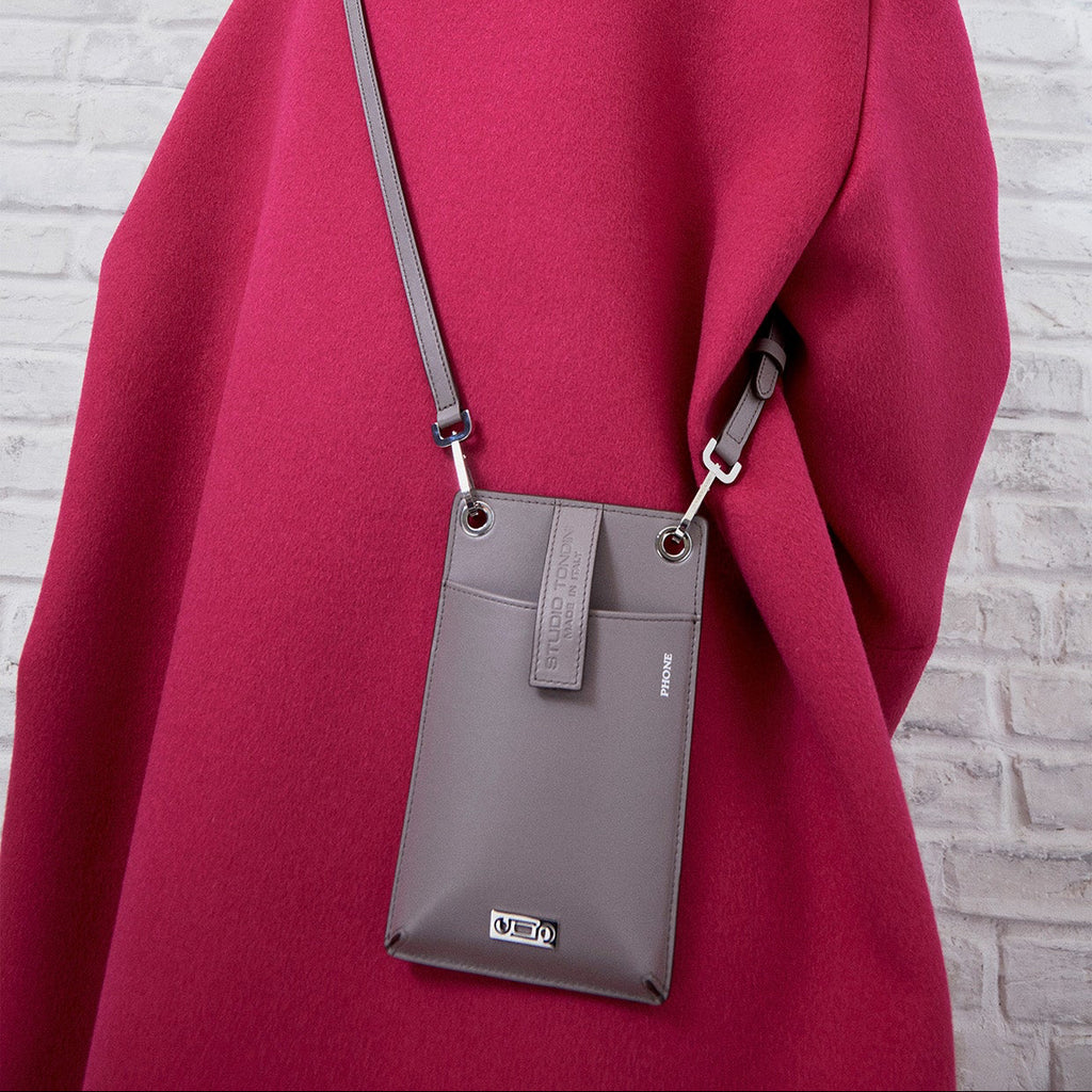 The Come Fly With Me! in Light Grey styled crossbody on model. Wide-angle image captures the bag worn on the back over a purple coat, in a minimal white brick studio setting.