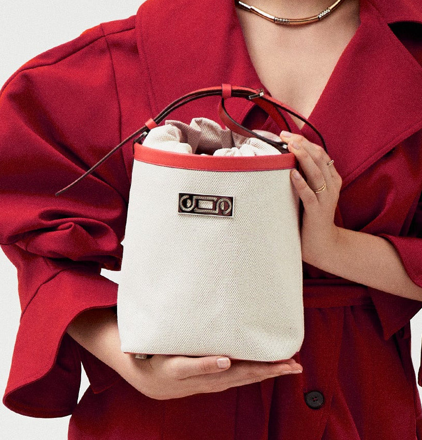 The Francesca Canvas Bucket Bag held by a model. Natural canvas with coral calf leather detailing, shown in proportion to torso and styled with a tailored coat.