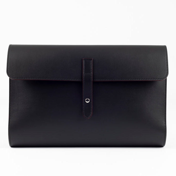 The Document Holder by Studio Tondini. Front view of black Italian leather bag with burgundy edge paint and button closure, showcasing clean lines and fine craftsmanship.